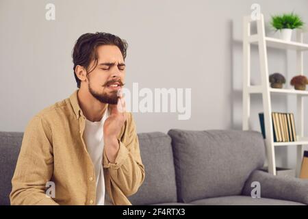 Giovane uomo che soffre di mal di denti acuti e di guancia a contatto con dolore Foto Stock