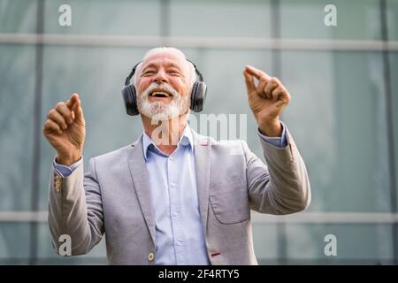 Ritratto all'aperto di un uomo d'affari anziano che sta godendo la musica sulle cuffie. Foto Stock
