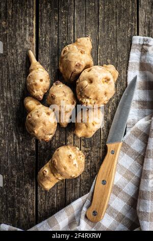 Carciofo di gerusalemme crudo. Radice vegetale di Topinambur su tavola di legno. Foto Stock