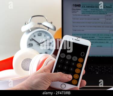 Kiev, marzo 2021. Mano con una calcolatrice sul telefono. Computer con modulo fiscale degli Stati Uniti 1040. Concetto di giorno fiscale. Foto Stock