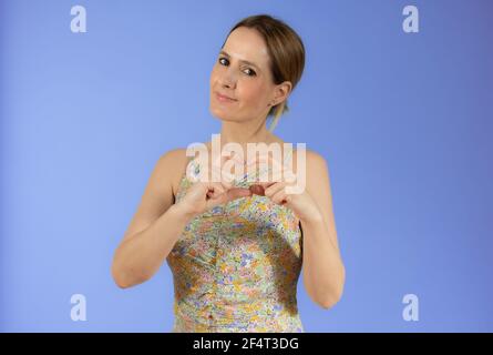 Donna caucasica in abito estivo è gesturing il segno d'amore con le mani sorridenti su sfondo viola. Foto Stock