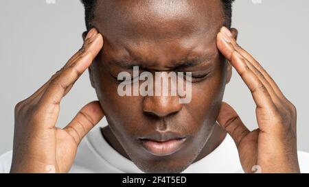 Esausto sconvolto l'uomo afroamericano che sente dolore che soffre di tempie di massaggio di emicrania. Studio. Foto Stock