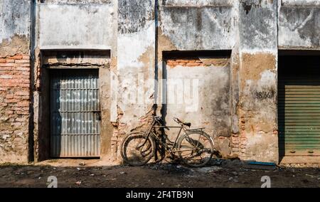 Murshidabad, Bengala Occidentale, India - Gennaio 2018: Una bicicletta che poggia contro un muro grugnoso delle rovine rustiche di una vecchia struttura nella città di Murshid Foto Stock