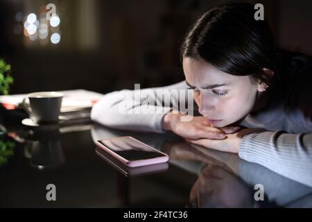 Triste donna in attesa di una chiamata cellulare che lo guarda di notte a casa Foto Stock