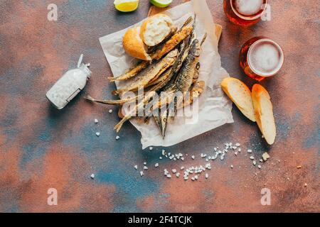 vista dall'alto di pesce fritto, birra, baguette, limone e sale su fondo di cemento Foto Stock