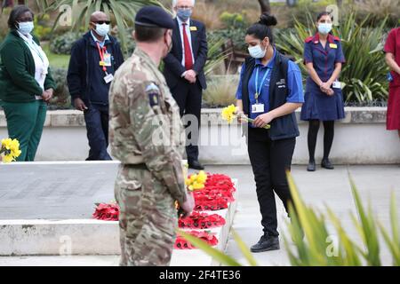 Un membro del personale porta fiori da collocare ai piedi della statua dell'infermiera della Guerra di Crimea Mary Seacole durante una cerimonia per osservare un minuto di silenzio al St Thomas' Hospital, nel centro di Londra, Come parte della Giornata Nazionale di riflessione, nell'anniversario del primo blocco nazionale per prevenire la diffusione del coronavirus. Data immagine: Martedì 23 marzo 2021. Foto Stock