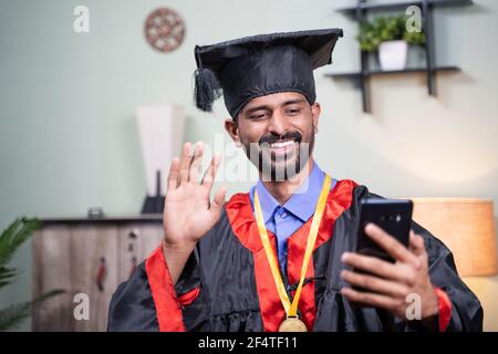 Studente che frequenta la sua cerimonia di laurea video online dal telefono cellulare in abito di laurea - concetto di celebrazioni virtuali, nuovo normale durante Foto Stock