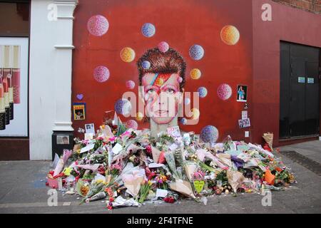 LONDRA, UK - GENNAIO 12 2016: Fiori posati dai fan di David Bowie al murale del musicista a Brixton dopo la sua morte Foto Stock