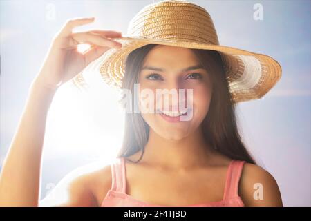 UNA GIOVANE DONNA ALLEGRA CHE TIENE IL CAPPELLO ESTIVO E CHE POSA DENTRO PARTE ANTERIORE DELLA TELECAMERA Foto Stock