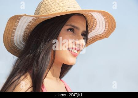 UNA GIOVANE DONNA CHE INDOSSA UN CAPPELLO ESTIVO CHE GUARDA FELICEMENTE SOPRA UNA GIORNATA ESTIVA Foto Stock