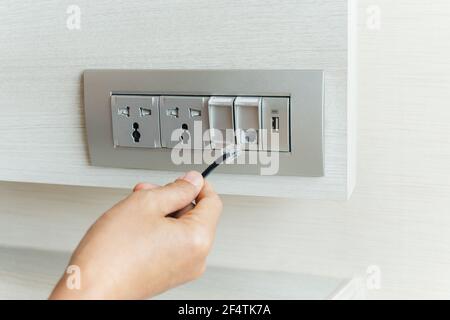 Uomo mano che tiene il cavo del Internet con il laptop sullo sfondo. Foto Stock