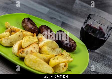 piatto salsicce patate e bicchiere di vino su fondo di legno Foto Stock