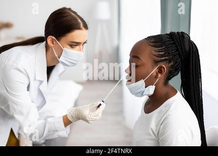 Medico che prende il campione di test PCR da donna nera potenzialmente infetta Foto Stock