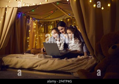 Madre con figlie prescolare che guardano il film su un computer portatile nei bambini tenda a casa Foto Stock