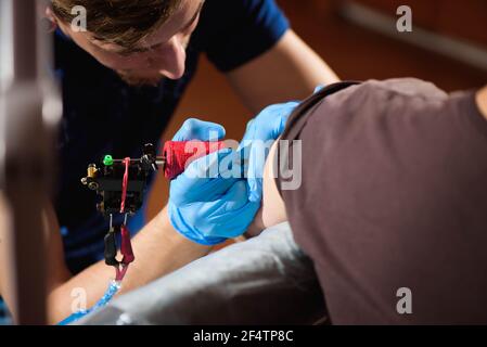 Tattoo Artist creando un tatuaggio su un uomo del braccio Foto Stock