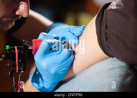 Tattoo Artist creando un tatuaggio su un uomo di braccio. Foto Stock