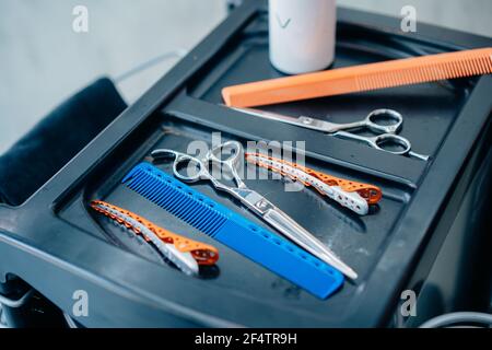 Primo piano di strumenti e attrezzature come forbici, pettine e clip conservati sul vassoio per il taglio dei capelli in un moderno parrucchiere barbershop Foto Stock