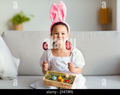 Asian Girl che indossa orecchie di coniglio di Pasqua che pongono uova di tenuta all'interno Foto Stock