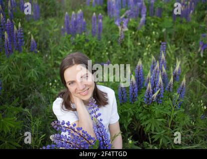 Bella donna sorridente 35 anni tra blu - viola lupini fiori selvatici nel prato. Ritratto femminile in natura. Detox digitale, week-end estivo. E Foto Stock