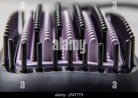 Setole nere e viola di una spazzola termica elettrica per lisciare i capelli durante la fotografia macro. Messa a fuoco selettiva. Immagine di sfondo Foto Stock