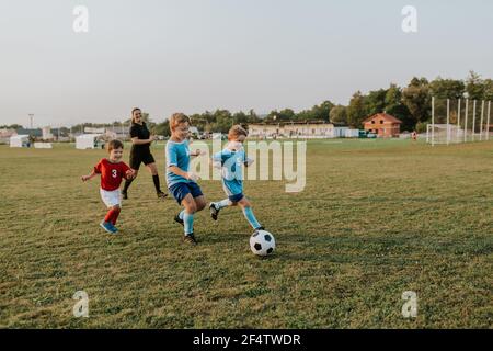 Bambini che giocano a calcio. Gruppo di giocatori di calcio felici che corrono dopo la palla sul campo. Foto Stock