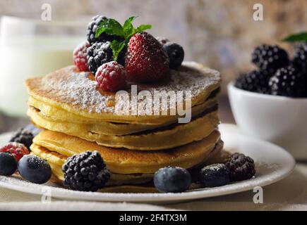 Un pasto completo con frittelle e frutti di bosco. Vista laterale. Un bicchiere di latte e una ciotola di more sullo sfondo. Foto Stock