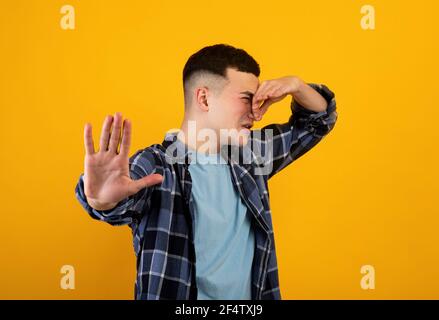 Giovane caucasico che chiude il naso, soffrendo di cattivo odore, gesturing STOP su sfondo arancione studio Foto Stock