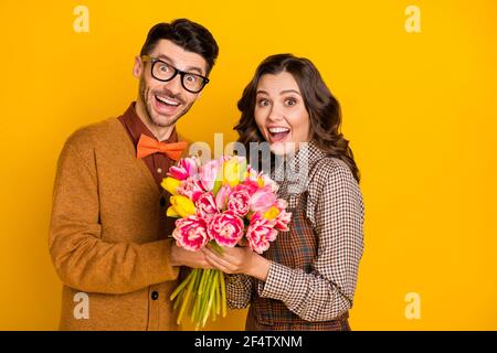 Foto di un giovane e una donna sbalorditi che tengono le mani vacanza fiori isolato su sfondo giallo luminoso Foto Stock