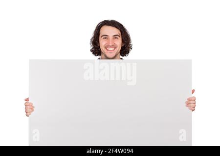 Giovane uomo soddisfatto che tiene un grande banner vuoto per la pubblicità. Felice ragazzo con un foglio vuoto per gli annunci di testo isolato su sfondo bianco con Foto Stock