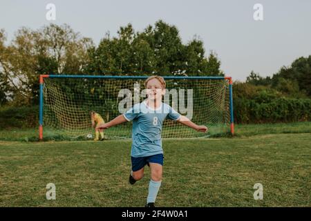 Bambini che giocano a calcio all'aperto sul campo. Lunghezza completa di gol punteggio ragazzo felice durante la partita di calcio amatoriale. Foto Stock