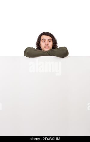 Giovane uomo malinconico, in piedi dietro un grande banner vuoto con messaggi copy space, guardando da parte pensieroso. Maschio pendente su un annuncio vuoto Foto Stock