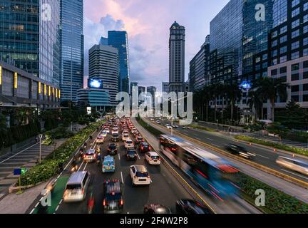 Il traffico, catturato dal movimento sfocato, si snoda lungo il viale principale fiancheggiato da grattacieli nel quartiere degli affari della capitale indonesiana. Foto Stock
