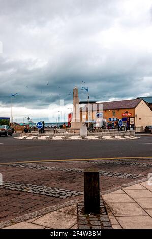 L'edificio classificato di grado 11, Seahouses War Memorial, si trova nel centro di una grande isola trafficata delimitata da un lato da negozi Foto Stock