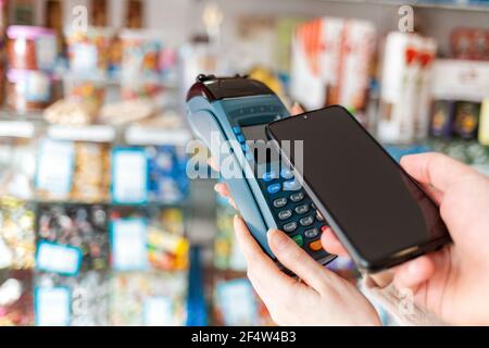 Le mani delle donne sono tenute da un terminale di pagamento e un uomo paga per un acquisto utilizzando uno smartphone. Spazio di copia. Il concetto di NFC, business e banking tr Foto Stock