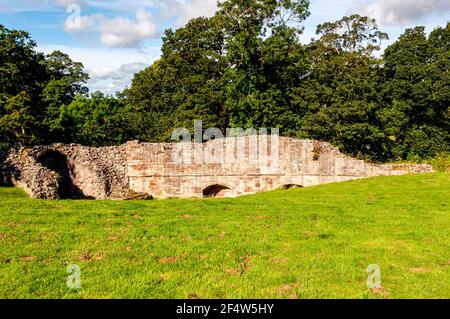 Le rovine di una porta nelle mura della tenda di Castello di Norham sotto un ripido pendio erboso coperto e circondato da alberi verdi Foto Stock