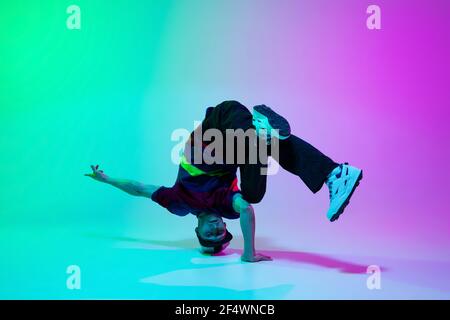 Bel ragazzo sportivo che balla hip-hop in abiti eleganti su sfondo sfumato colorato nella sala da ballo in luce al neon. Foto Stock