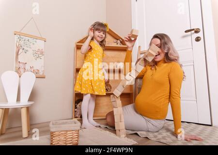 Una donna incinta gioca nella stanza dei bambini con sua figlia. Costruiscono una torre di blocchi di legno. Foto Stock