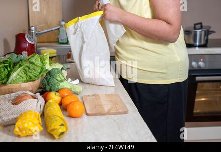 Donna irriconoscibile in T-shirt gialla che mette le verdure in borsa di cotone Foto Stock