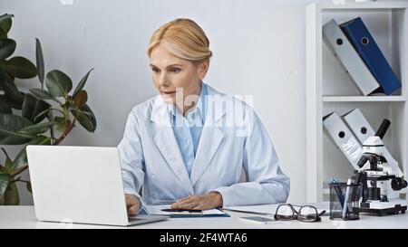 medico concentrato in camice bianco che lavora su computer portatile in ospedale Foto Stock