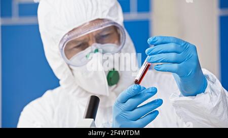virologo che trattiene la provetta con il campione di sangue in laboratorio, sfondo sfocato Foto Stock