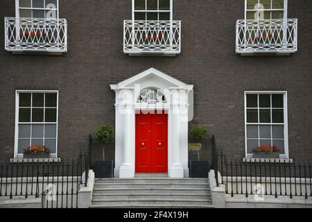 Edificio in vecchio stile georgiano in mattoni, con una porta d'ingresso luminosa rossa e finestre simmetriche su Merrion Square Dublin, Irlanda. Foto Stock