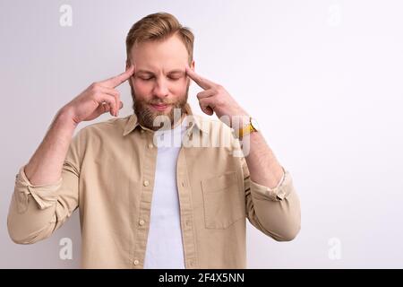 ragazzo che tiene le dita sui templi, cercare di ricordare, pensando alla domanda, espressione pensiva. Ragazzo caucasico bearded con faccia premurosa. Dubbio concep Foto Stock