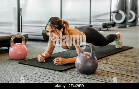 Donna asiatica dello sport in palestra, allenamenti atleti, pesi di sollevamento allenamento, tavola e spingere in su. Tatuaggio tailandese ragazza Foto Stock