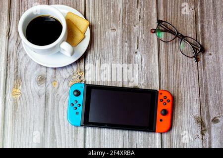 Uno schermo di interruttore Nintendo posto su un tavolo di legno accanto a un caffè e bicchieri Foto Stock