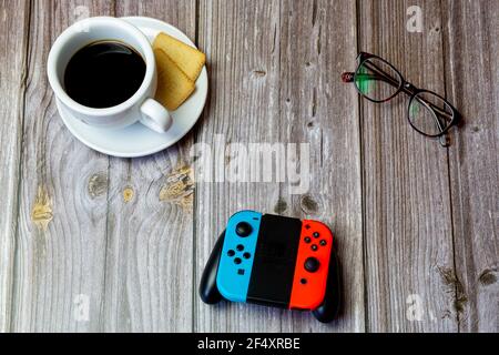 Un controller di commutazione Nintendo posizionato su un tavolo di legno accanto a un caffè e bicchieri Foto Stock