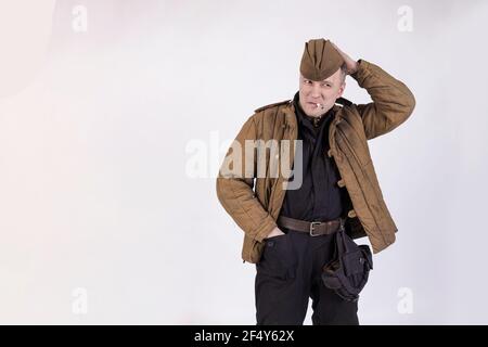 Ritratto di un attore maschile in uniforme militare di un tankman russo del periodo della seconda guerra mondiale per fumare una sigaretta su uno sfondo bianco Foto Stock