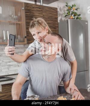 felice coppia sposata, scattando foto l'una dell'altra al telefono, mostrando la loro lingua cosparsa di farina mentre cucinando in cucina. gioie di famiglia Foto Stock
