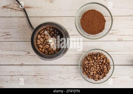 I chicchi di caffè nel mulino e il caffè messo a terra nel ciotola sullo sfondo in legno vista dall'alto Foto Stock