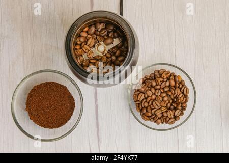 Vista dall'alto dei chicchi di caffè nel tritatutto e del terreno caffè nel recipiente di vetro sul tavolo di legno Foto Stock