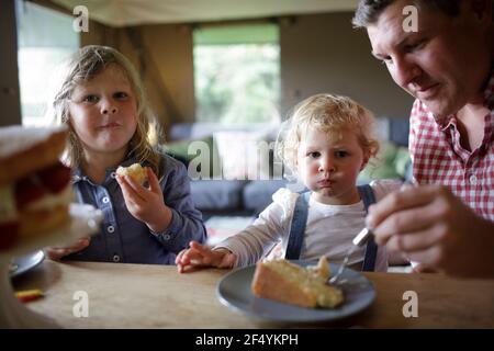 Padre e figlie mangiano torta al tavolo da pranzo Foto Stock